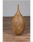 Mustard glazed ceramic vase with tapered spout on wooden floor beside a light gray wall indoors.