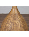 Close-up of mustard glazed ceramic vase with tapered spout, handmade Thai style, on wood surface.