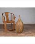 Wooden chair and mustard-glazed Thai ceramic vase on wood floor next to white brick wall indoors.