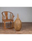Wooden chair and mustard-glazed Thai ceramic vase on wood floor next to white brick wall indoors.