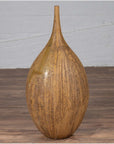 Mustard yellow ceramic vase with tapered spout on wooden floor near white brick wall indoors.