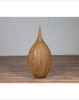 Mustard yellow ceramic vase with tapered spout on wooden floor against white brick wall indoors.