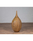 Mustard yellow ceramic vase with tapered spout on wooden floor against white brick wall indoors.