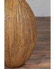 Mustard yellow ceramic vase with tapered spout on wooden floor against white wall, handmade Thai style.