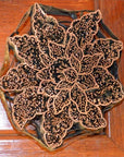 Close-up of a copper batik ink block with floral pattern on a wooden surface.