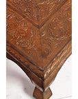 Close-up of copper coffee table corner with embossed floral and leaf patterns on the metal surface and edges.