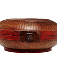 Close-up of a woven basket with a red band and brass lock, closed and resting on a flat surface.