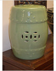Green celadon porcelain garden seat with vintage-style decorative cut-outs, displayed indoors on wood floor.