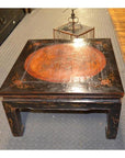 Black lacquer wood Kang table with horse hoof feet, painted Asian-style design, on a patterned floor.