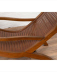 Wooden lounge chair with curved seat and slats, on wooden floor against a white wall indoors.