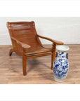 Brown wood Indonesian lounge chair with curved seat on wooden floor next to tall ceramic vase indoors.