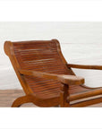 Brown wood lounge chair with curved seat and slats, placed indoors by a white brick wall on a wooden floor.