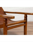 Close-up of a brown wooden lounge chair with curving seat and slats on a wooden floor against a white wall indoors.
