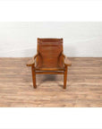 Wooden Dutch Colonial Indonesian lounge chair with curved seat and slats on a wooden floor by a white brick wall.