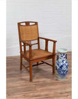 Brown Javanese teak armchair with rattan seat next to blue and white vase on wooden floor.