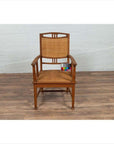 Brown teak and rattan Dutch Colonial Javanese armchair with triglyph motifs on wooden floor by white brick wall.