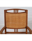Brown teak and rattan Dutch Colonial Javanese armchair with triglyph motifs, against a white brick wall background.