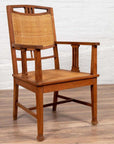 Brown teak and rattan Dutch Colonial Javanese armchair with triglyph motifs on wooden floor by a white brick wall.