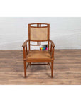 Brown teak and rattan Dutch Colonial Javanese armchair, color chart on seat, on wood floor against white brick wall.