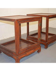 Brown Elmwood side tables with glass sides and hinged doors, positioned side by side on a gray floor against a white wall.