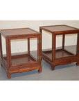 Two elmwood side tables with open sides and simple design on a gray floor against a white wall.