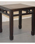 Brown elmwood stool with burl inlay and carved legs on a gray floor against a white wall.