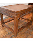 Brown wood Elmwood stool or table with carved sides, cane top, and sturdy legs on a wooden floor.