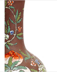 Close-up of white ceramic flower vase with colorful floral patterns and green leaves on a white background.