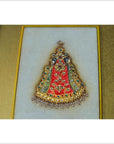 Close-up of framed Indian artwork with red, green, and blue enamel, gemstones, pearls on white fabric.