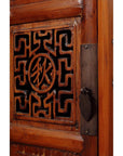 Close-up of dark wood Chinese cabinet with geometric fretwork carvings, butterfly hardware, and circular central symbol.