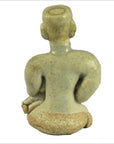 Brown glazed terracotta fertility doll, seated with topknot, viewed from behind showing bare back and bent arms.
