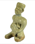Close-up of a glazed terracotta fertility doll, kneeling with hat, holding object across chest.