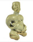 Brown glazed terracotta miniature fertility doll, seated with visible facial features and a textured rounded object, close-up.