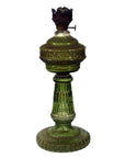 Close-up of antique green glass oil lamp with ornate embossed details, metal burner top, and ribbed pedestal.