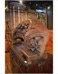Brown wood arch sculpture with hand-carved floral designs on a stand, displayed in an antique shop setting.