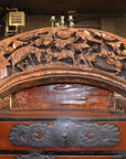 Brown wood arch sculpture with hand-carved animal and floral motifs on a dark antique chest.