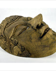Close-up of a hand carved Balinese wooden theater mask with a serene face and textured details, lying on its side.