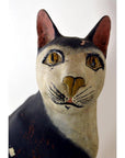 Close-up of hand carved black and white cat figurine with yellow eyes, detailed features, wood material visible.
