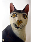 Close-up of hand carved black and white cat figurine with yellow eyes, detailed features, wood material visible.