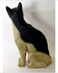 Rear view of a hand-carved cat statue with visible paint wear, wood material, on a white surface.