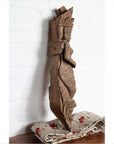 Hand carved brown stone Hindu deity statue on floral fabric in front of a white brick wall.