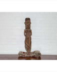 Brown wood statue of Hindu deity on patterned cloth, set against a white brick wall indoors.