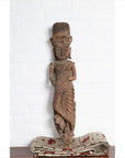 Brown wood statue of Hindu deity, hand carved from Gujarat, displayed on cloth against a white brick wall indoors.