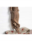 Brown wood carved statue of Hindu deity from Gujarat seated on floral fabric against a white wall indoors.
