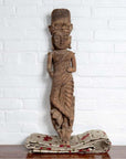 Brown hand-carved wood statue of Hindu deity with headdress on patterned fabric.