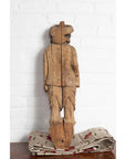Brown hand-carved wood statue of mother and child on patterned cloth, white brick wall background.