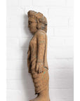 Brown hand carved wood mother and child statue from Gujarat, side view, beside white brick wall.