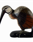 Brown wooden hand carved Indonesian kiwi bird with long beak, detailed feathers, and black base on display.