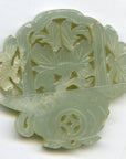 Close-up of pale green jade medallion with hand-carved floral and leaf patterns, 2"x2"x1/4", intricate cut-outs.