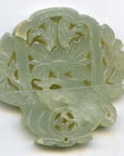 Green jade medallion with hand-carved floral and leaf designs, displayed on a steel plate, close-up view.